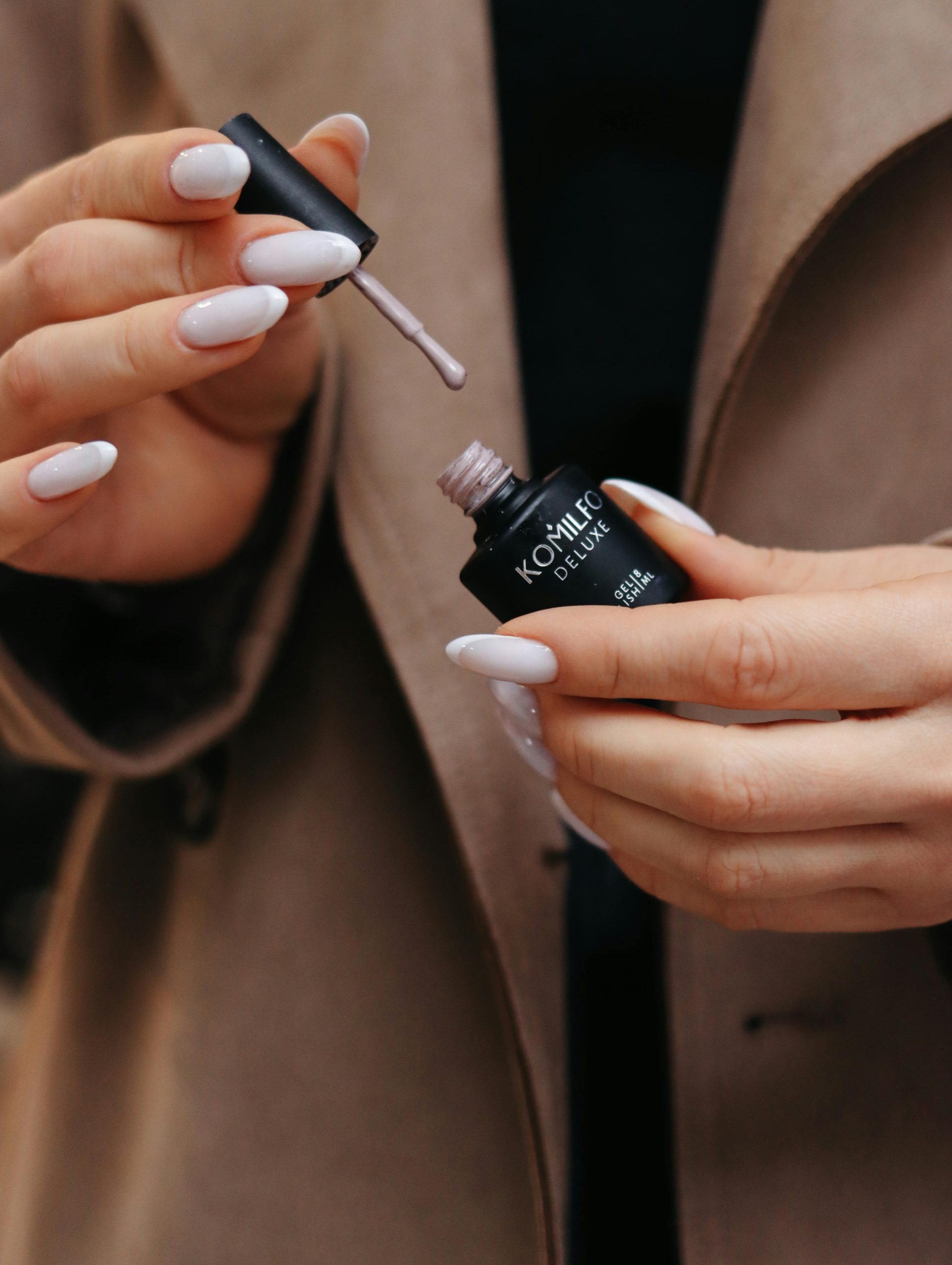 Close-up d'une femme appliquant du vernis à ongles nude sur ses ongles.