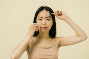 Asian woman utilisant un rouleau facial pour les soins de la peau et l'auto-soin dans un cadre studio.