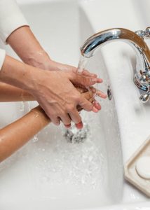 From above of crop unrecognizable mum washing hands of child with clear warm running water in white washbasin Enfant non identifiable lavé les mains par une mère sous une eau claire et chaude dans un lavabo blanc vu d'en haut