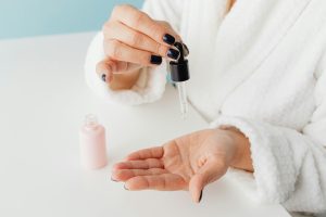 Close-up of a woman applying skincare serum from a dropper onto her hand in a studio setting. Gros plan d'une femme appliquant un sérum de soin de la peau d'un compte-gouttes sur sa main dans un environnement studio.