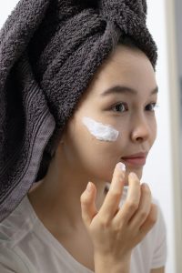 Close-up of a woman applying face cream, emphasizing skincare routine and self-care habits. Gros plan d'une femme appliquant une crème pour le visage, mettant l'accent sur la routine de soins de la peau et les habitudes d'autosoins.