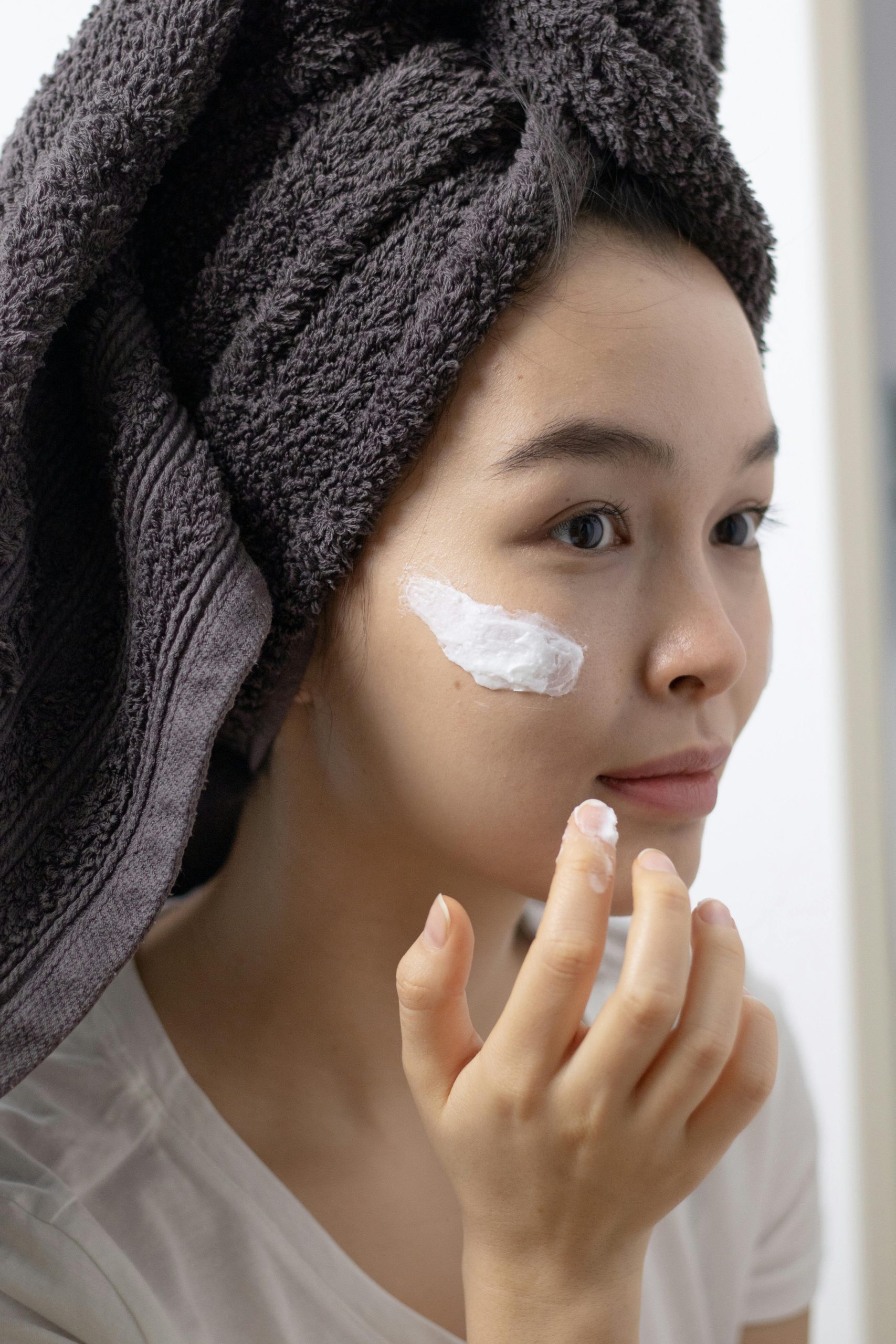 Close-up of a woman applying face cream, emphasizing skincare routine and self-care habits. Gros plan d'une femme appliquant une crème pour le visage, mettant l'accent sur la routine de soins de la peau et les habitudes d'autosoins.
