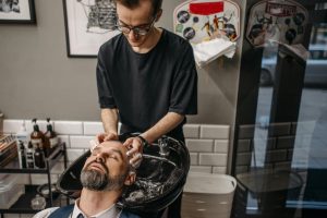 Barber washing client's hair at shampoo station in modern salon setting. Un barbier lave les cheveux du client à la station de shampooing dans un salon moderne.