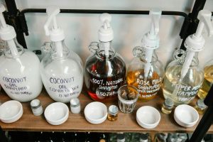 Collection of big dispensers of various multicolored shampoo placed near glass jars and white bowls on wooden shelf Collection de grands distributeurs de shampooing multicolore placés près de bocaux en verre et de bols blancs sur une étagère en bois