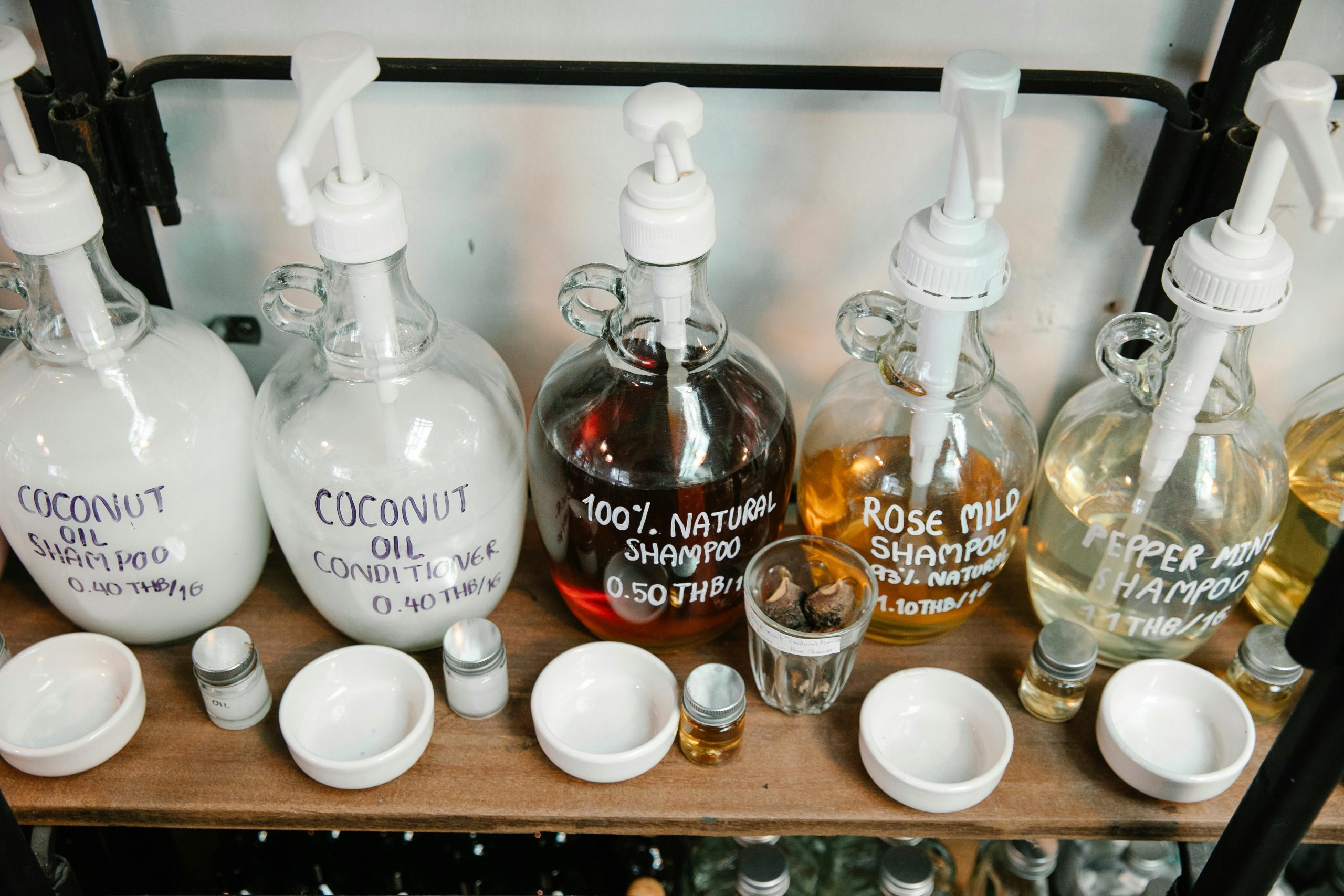Collection of big dispensers of various multicolored shampoo placed near glass jars and white bowls on wooden shelf Collection de grands distributeurs de shampooing multicolore placés près de bocaux en verre et de bols blancs sur une étagère en bois