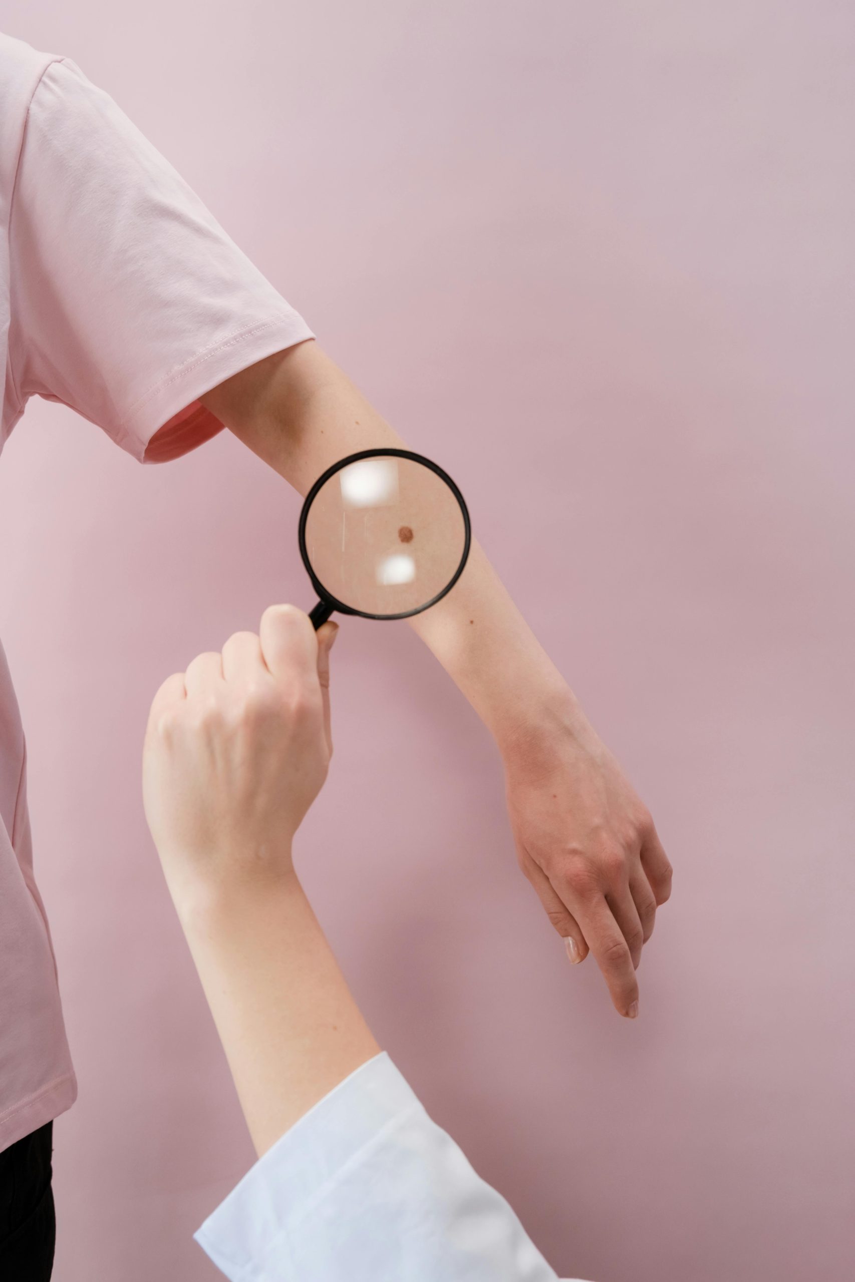 Close-up of a dermatologist examining skin with a magnifier on a pink background. Gros plan d'un dermatologue examinant la peau avec une loupe sur fond rose.