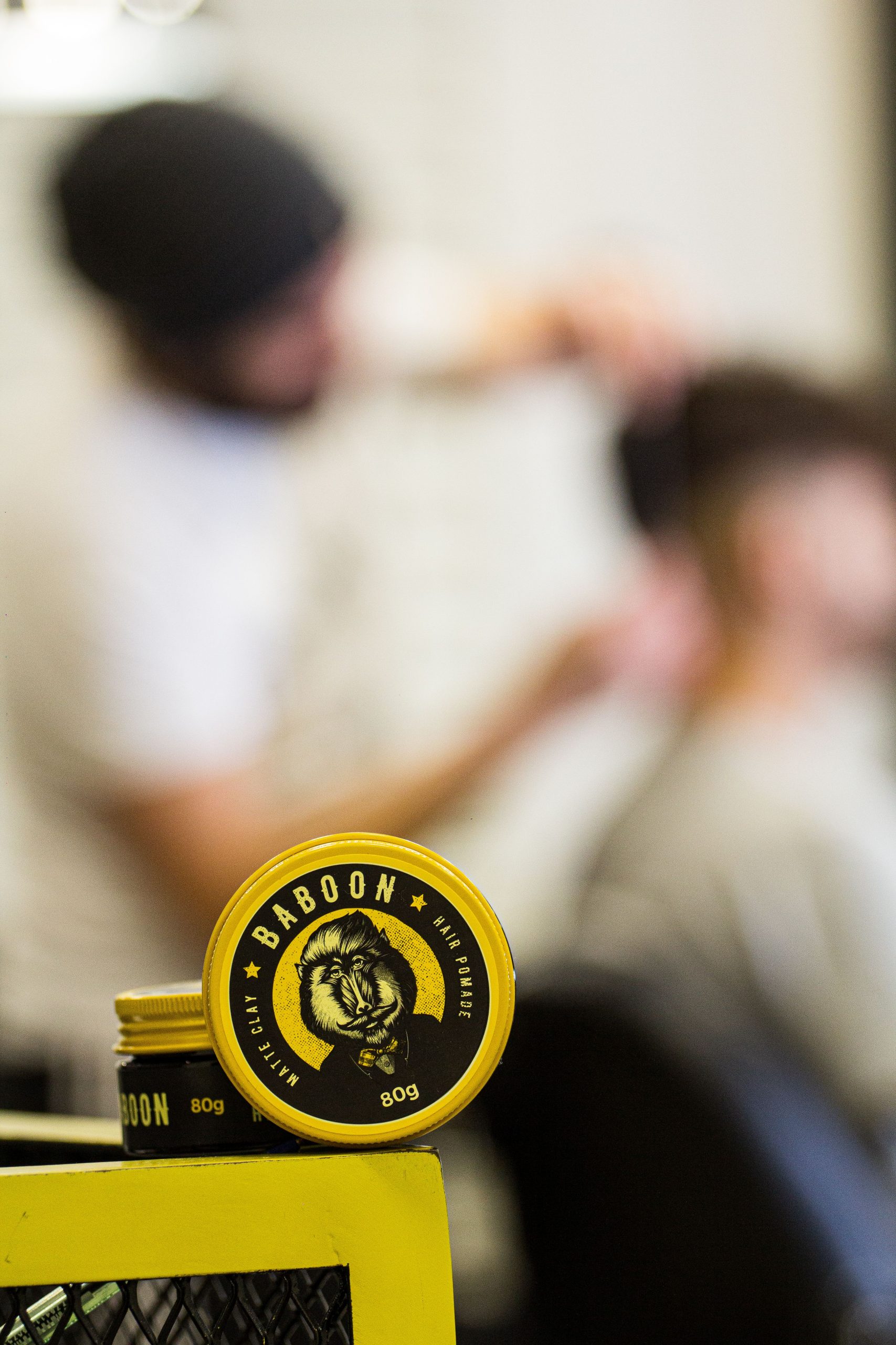 Close-up of Baboon hair product in a barbershop with stylist and client in background. Gros plan du produit capillaire Baboon dans un salon de coiffure avec le coiffeur et le client en arrière-plan.