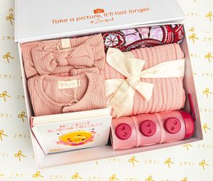 Adorable boîte cadeau pour bébé avec vêtements roses, un livre de puzzle et des bacs de rangement.
