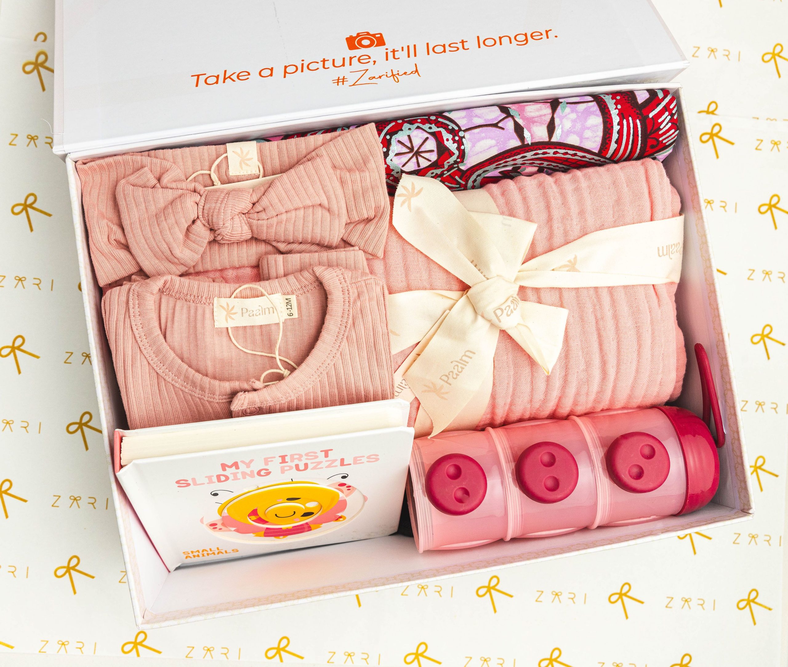 Adorable boîte cadeau pour bébé avec vêtements roses, un livre de puzzle et des bacs de rangement.