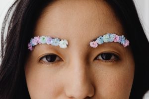 A close-up portrait of a woman with floral eyebrows, showcasing creative makeup art. Un portrait en gros plan d'une femme aux sourcils floraux, mettant en avant un art du maquillage créatif.