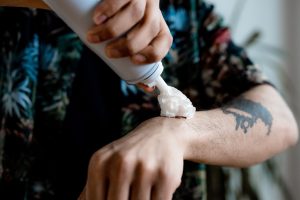A person applying whipped cream onto a tattooed arm, close-up view. Une personne appliquant de la crème fouettée sur un bras tatoué, vue rapprochée.