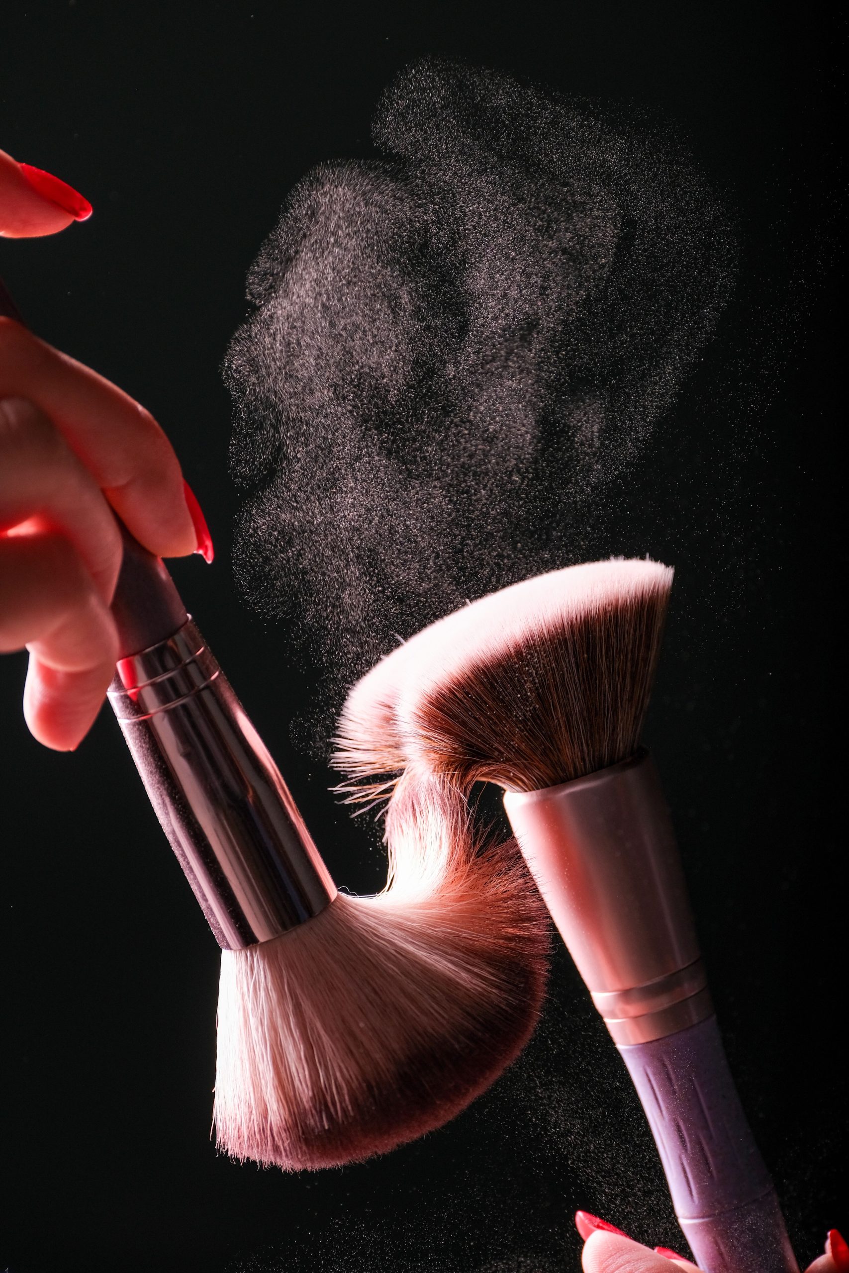 Dynamic studio shot of makeup brushes creating a powder burst against a dark background. Prise de vue en studio dynamique de pinceaux de maquillage créant une explosion de poudre sur un fond sombre.