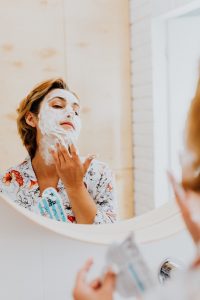 Woman applying face mask with foam in front of the bathroom mirror for a skincare routine. Femme appliquant un masque facial mousseux devant le miroir de la salle de bain pour une routine de soins de la peau.