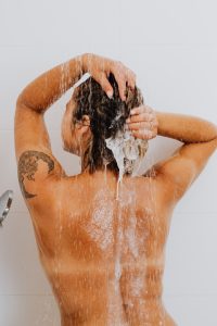Rear view of a woman washing her hair in the shower, showcasing a tattoo and emphasizing hygiene. Vue arrière d'une femme se lavant les cheveux sous la douche, mettant en avant un tatouage et soulignant l'hygiène.
