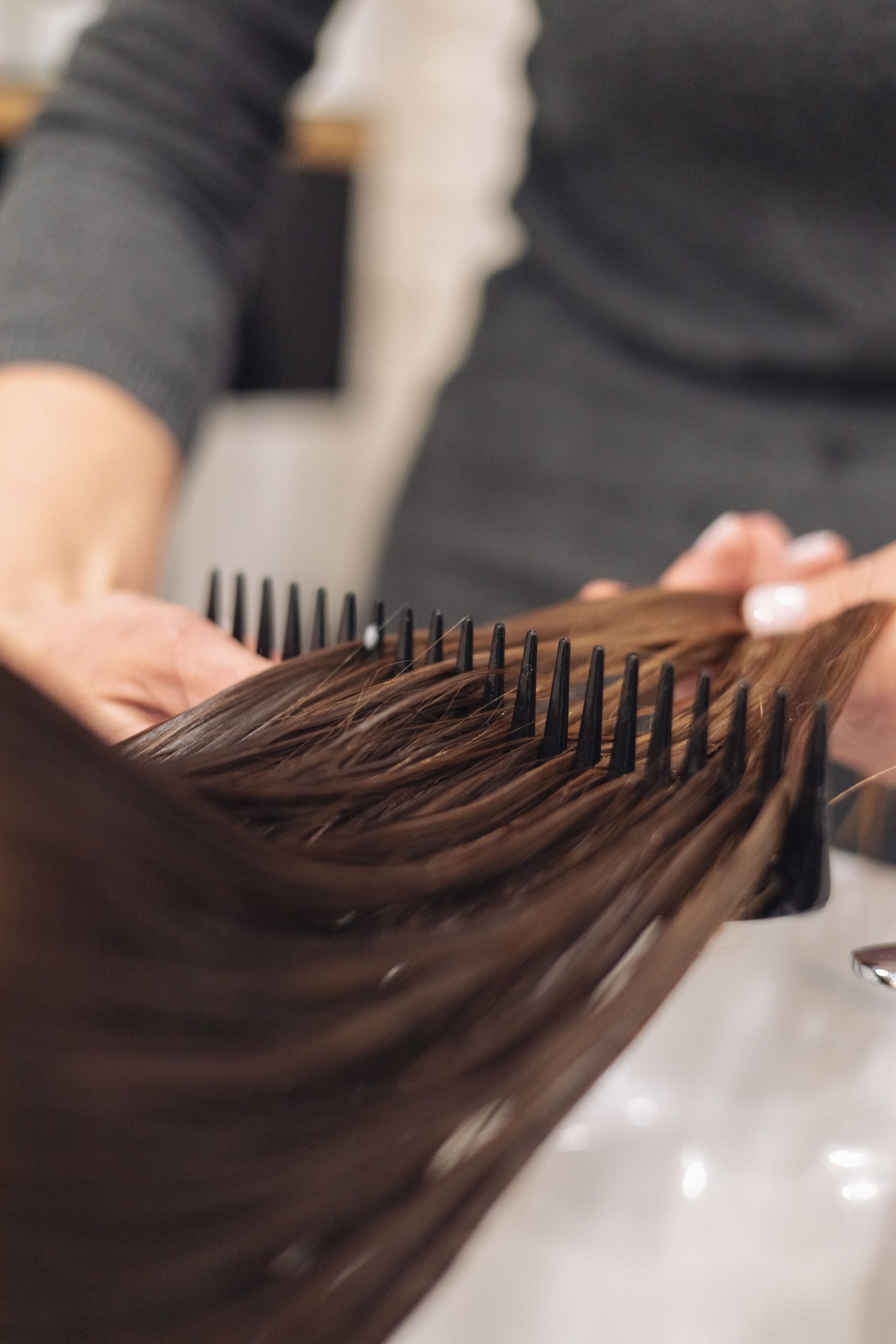A hairdresser skillfully combs wet hair, focusing on smooth styling in a salon setting. Une coiffeuse peigne habilement les cheveux mouillés, en mettant l'accent sur un coiffage lisse dans un salon de coiffure.