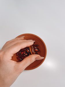 Close-up shot of a hand holding vitamin pills out of a terracotta bowl on a white background. Gros plan d'une main tenant des comprimés de vitamines sortant d'un bol en terre cuite sur un fond blanc.