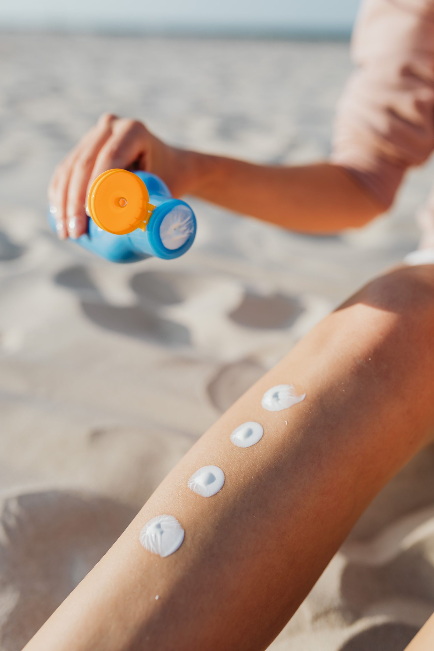 Woman applying sunscreen lotion on leg at the beach. Summer skincare routine for sun protection outdoors. Une femme applique de la crème solaire sur sa jambe à la plage. Routine de soins de la peau d'été pour la protection solaire en plein air.