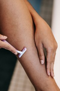 Femme éthique anonyme recadrant l'épilation des jambes avec un rasoir en plastique dans la salle de bain à la maison en journée