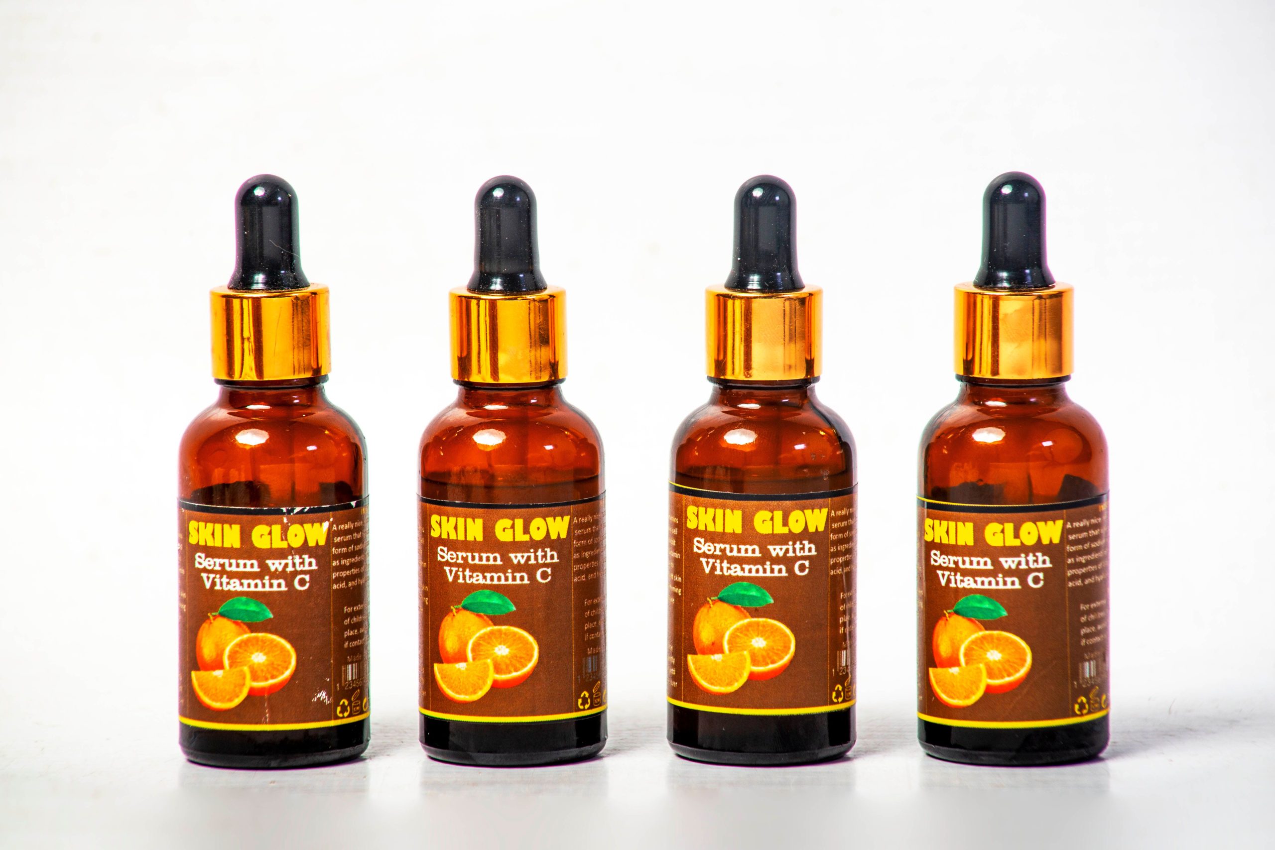 Four Vitamin C serum bottles arranged on a white background for skincare. Quatre flacons de sérum à la vitamine C arrangés sur un fond blanc pour les soins de la peau.