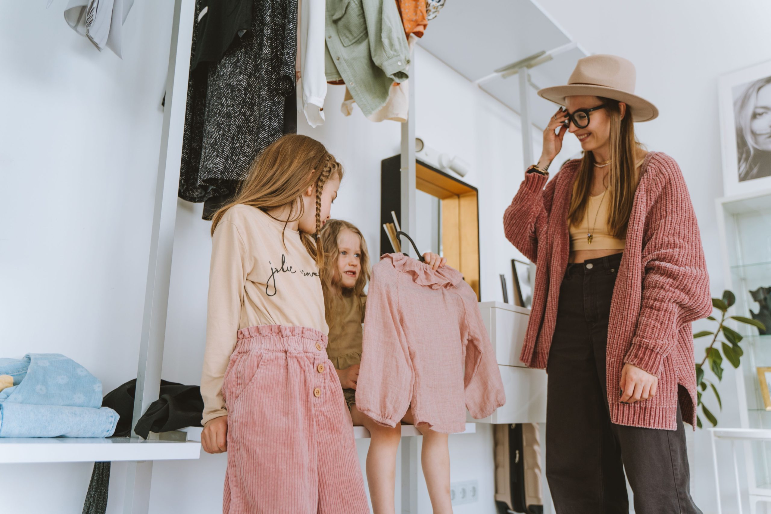 A mother and her daughters choose outfits in a stylish, cozy home setting. Une mère et ses filles choisissent des tenues dans un cadre élégant et confortable à la maison.