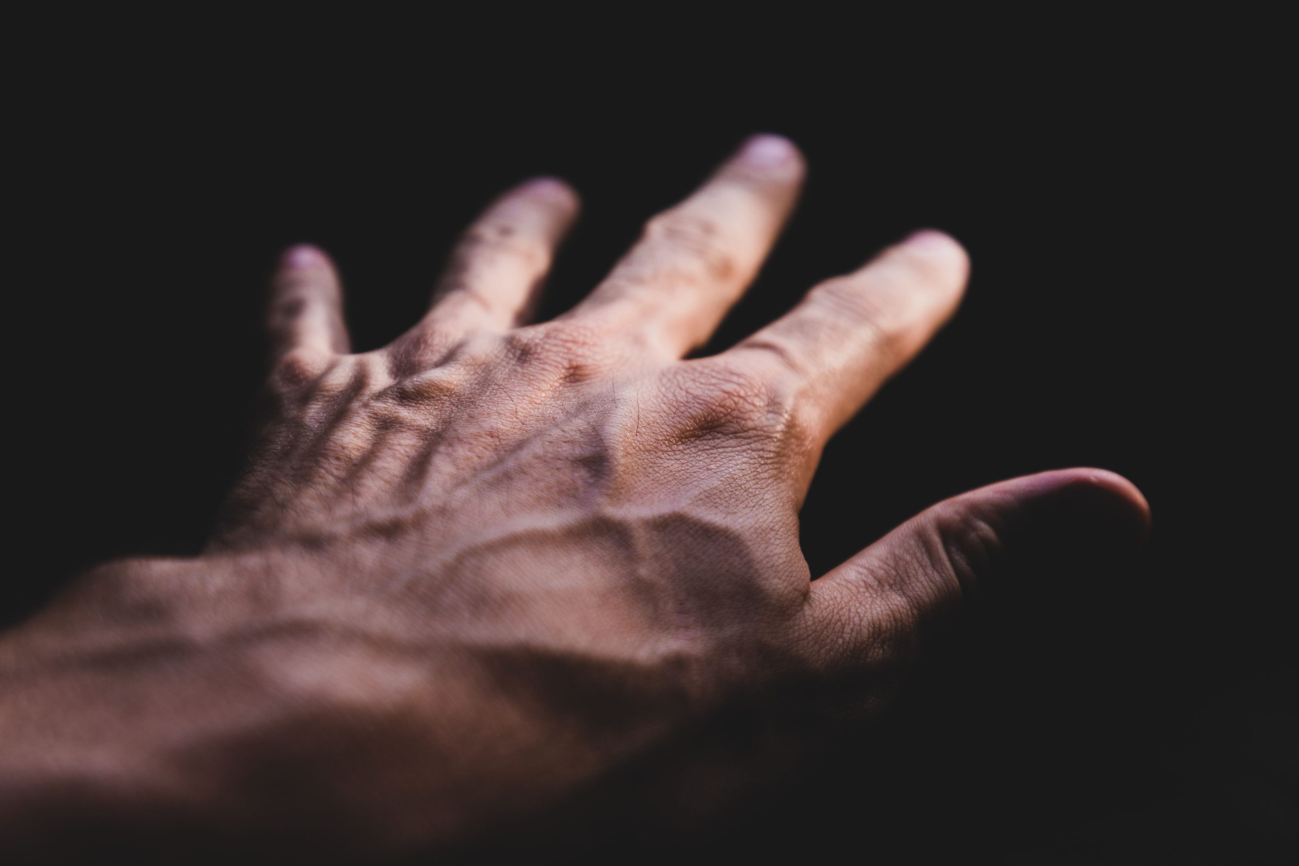 Detailed image of a human hand showing prominent veins against a dark background. Image détaillée d'une main humaine montrant des veines proéminentes sur un fond sombre.
