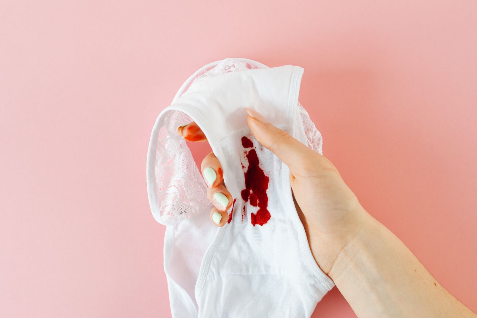 Gros plan sur une main tenant des sous-vêtements blancs avec une tache menstruelle sur fond rose
