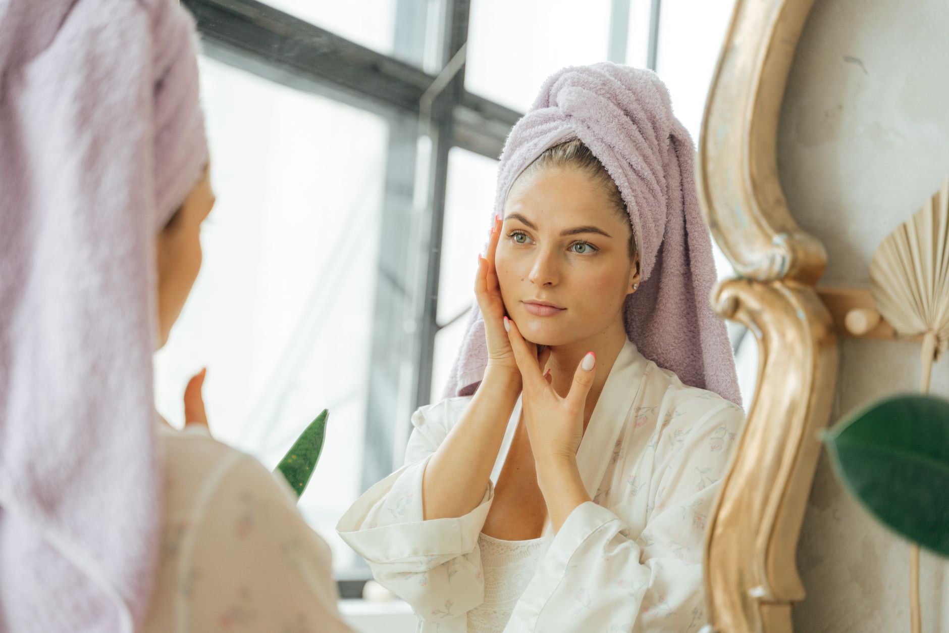 Femme en peignoir touchant son visage devant un miroir