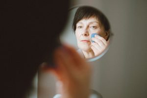 Femme senior appliquant son fond de teint devant un miroir