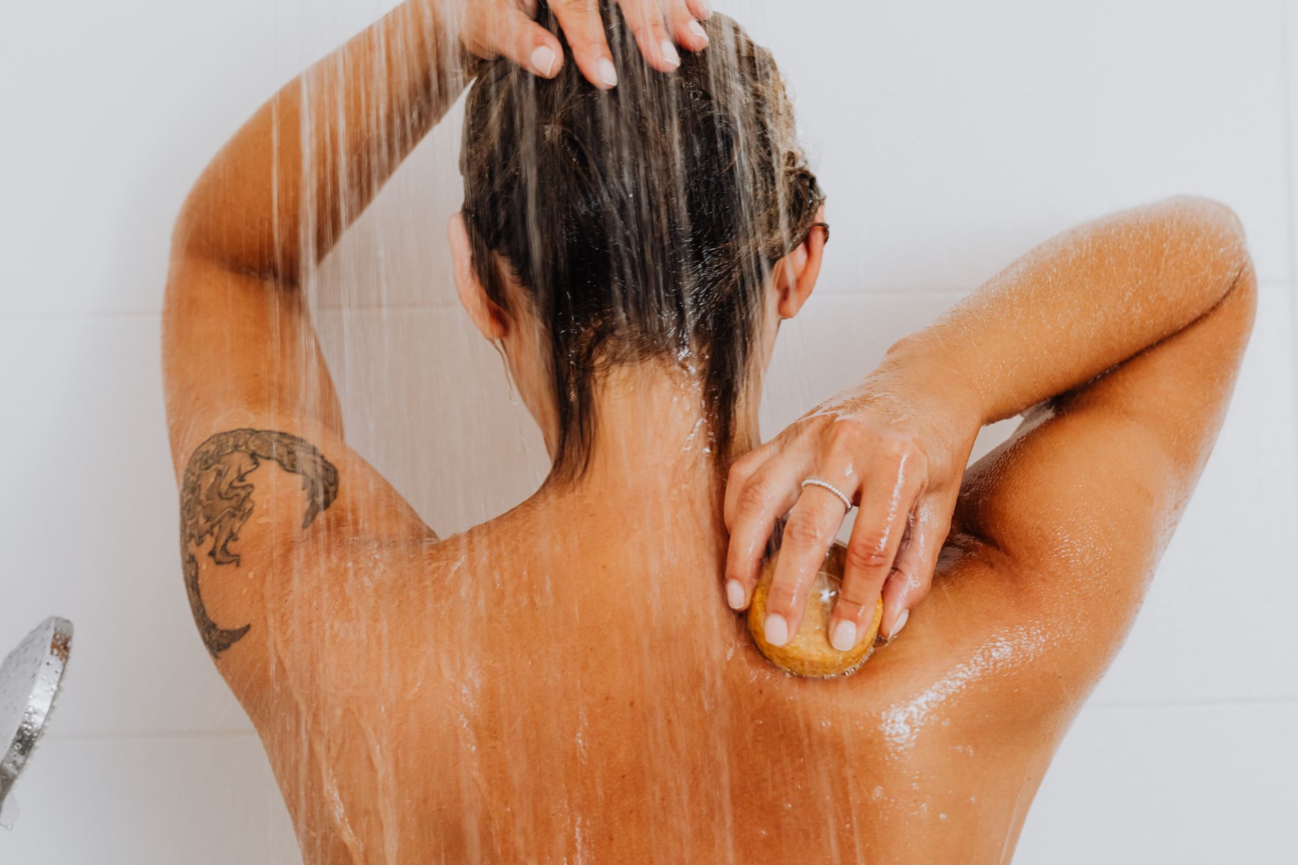 Dos d’une femme sous la douche avec un shampoing solide