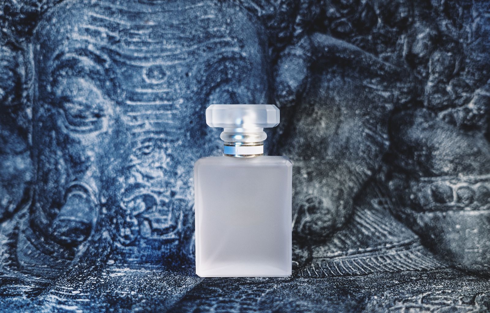 Flacon de parfum givré posé devant une sculpture texturée