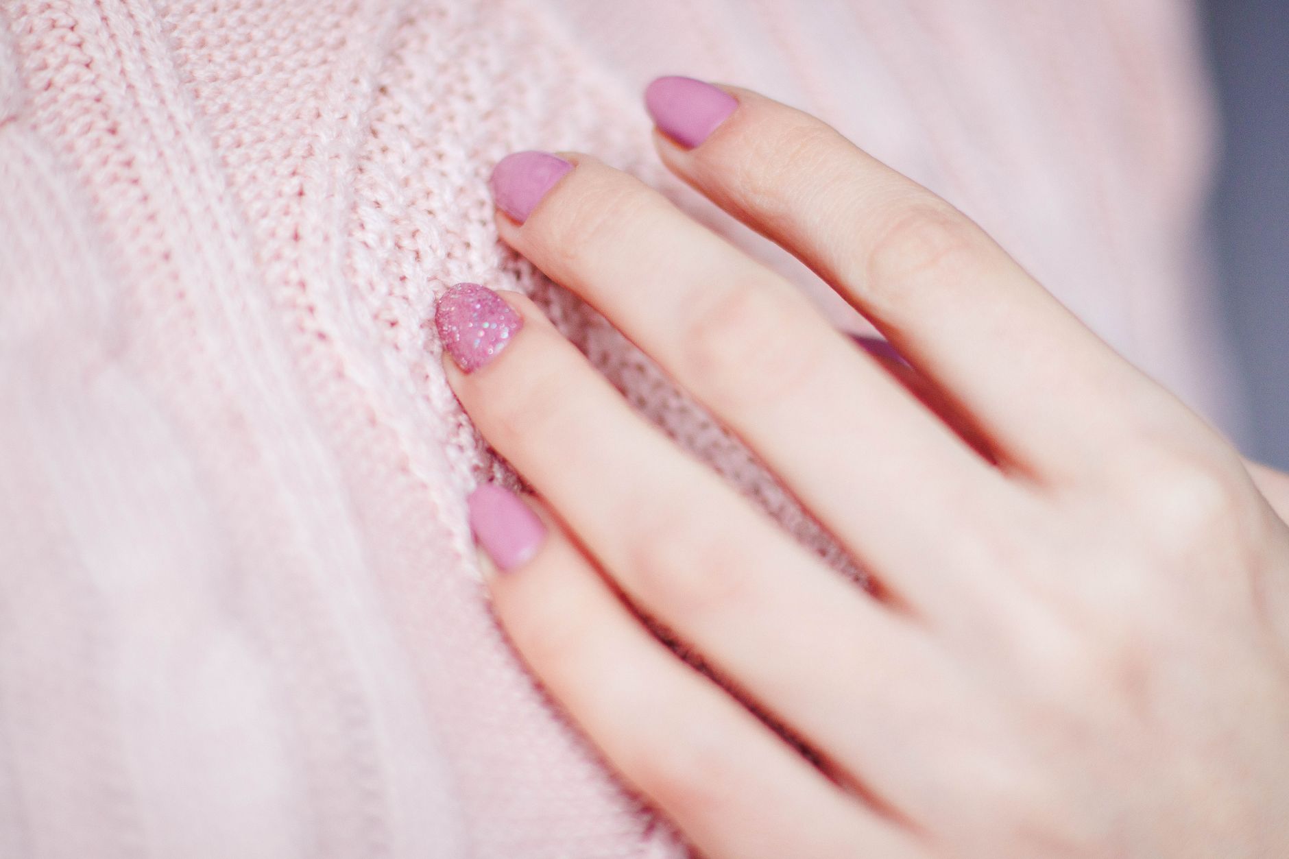 Main avec une manucure rose posée sur un tricot